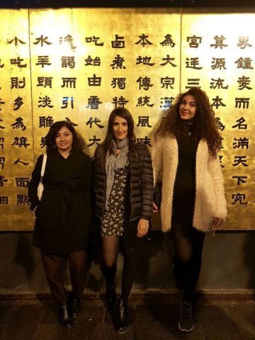 Enza with her friends in Beijing in front of a wall full of Chinese characters